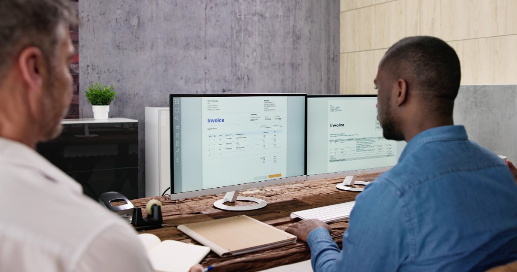 Analysts reviewing invoices on dual monitors